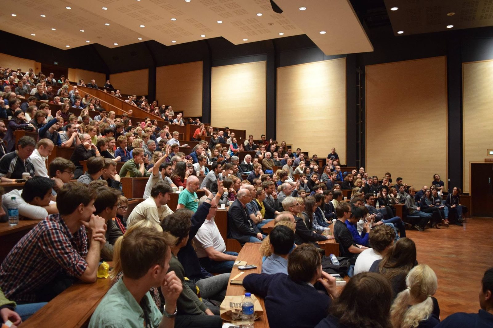 A packed lecture theatre, hands raised for questions, at a CUPS talk